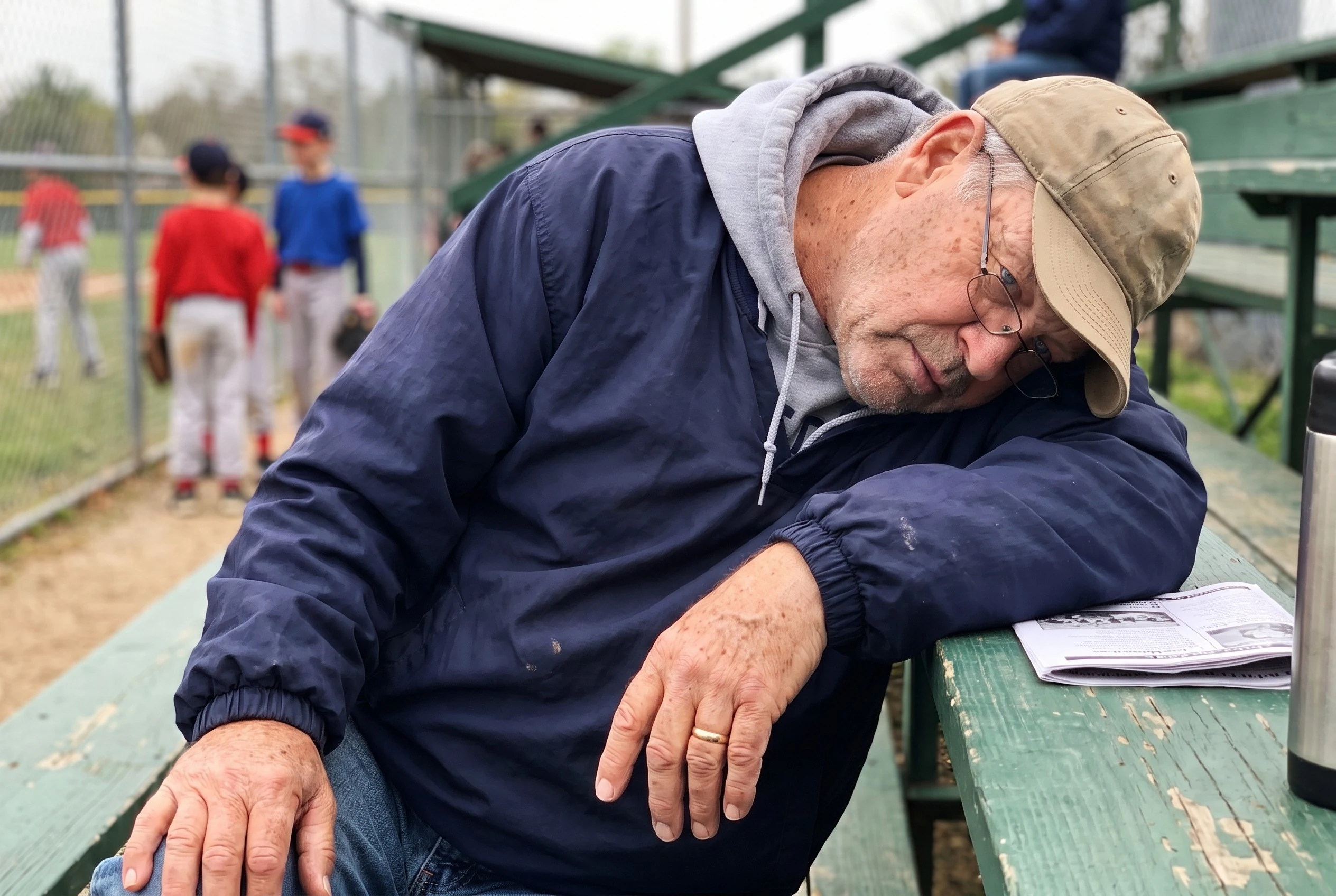 Walt asleep chin-on-chest in wooden bleachers, shot by daughter from row behind, overcast