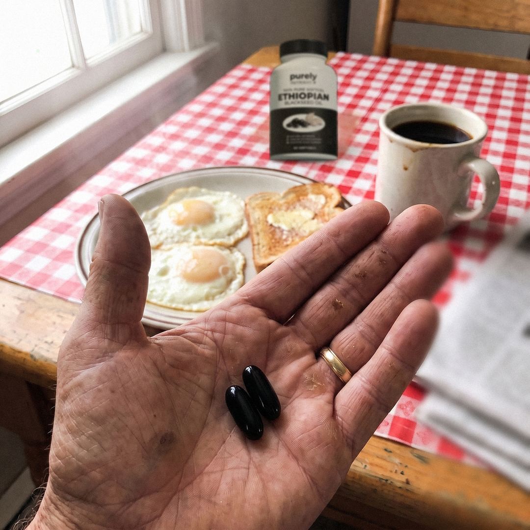 real bottle on breakfast table, 2 black softgels in palm